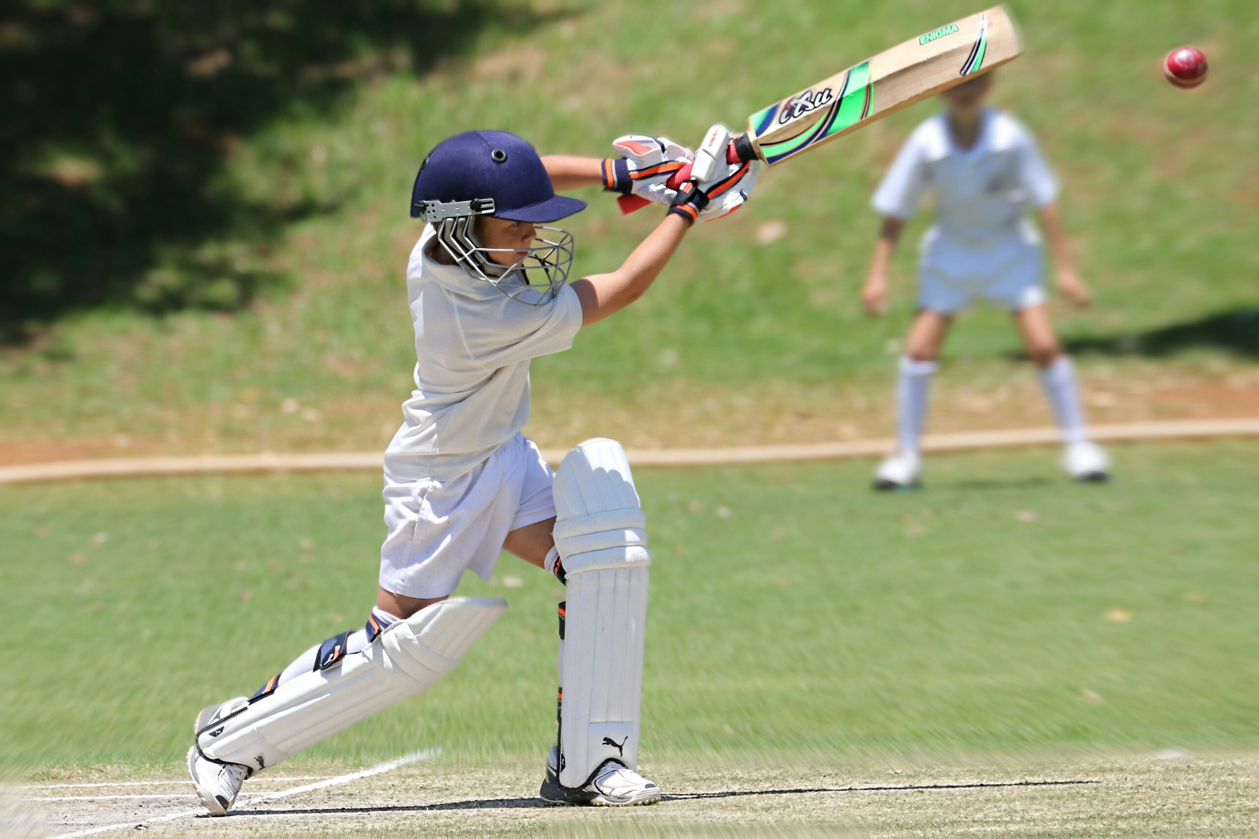 Young cricketer in white gear executing a sweep shot on a sunny day.